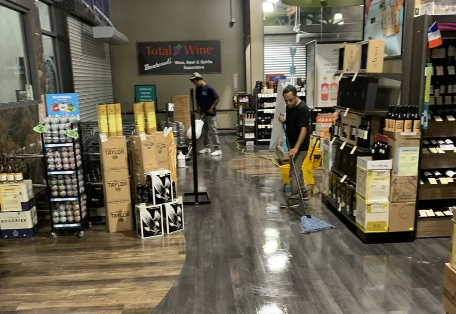 Two cleaners using a mop and floor machine in a store aisle
