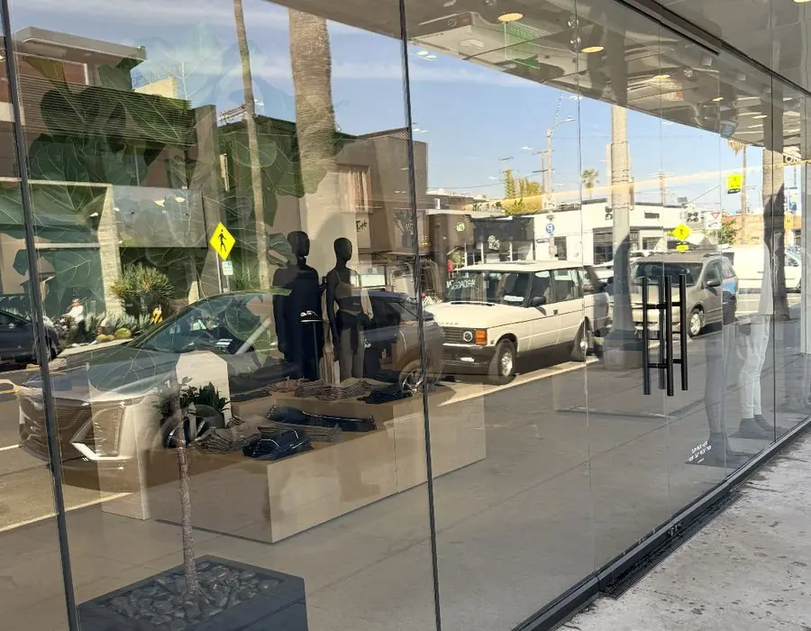 Full-height storefront glass with door handles, clothing displays and street reflections